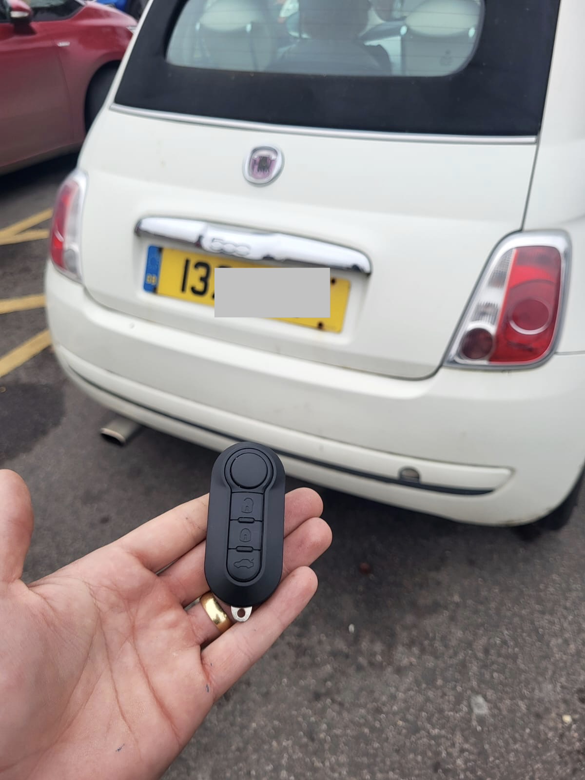 Three-button Fiat flip remote key held in front of a white Fiat 500 convertible
