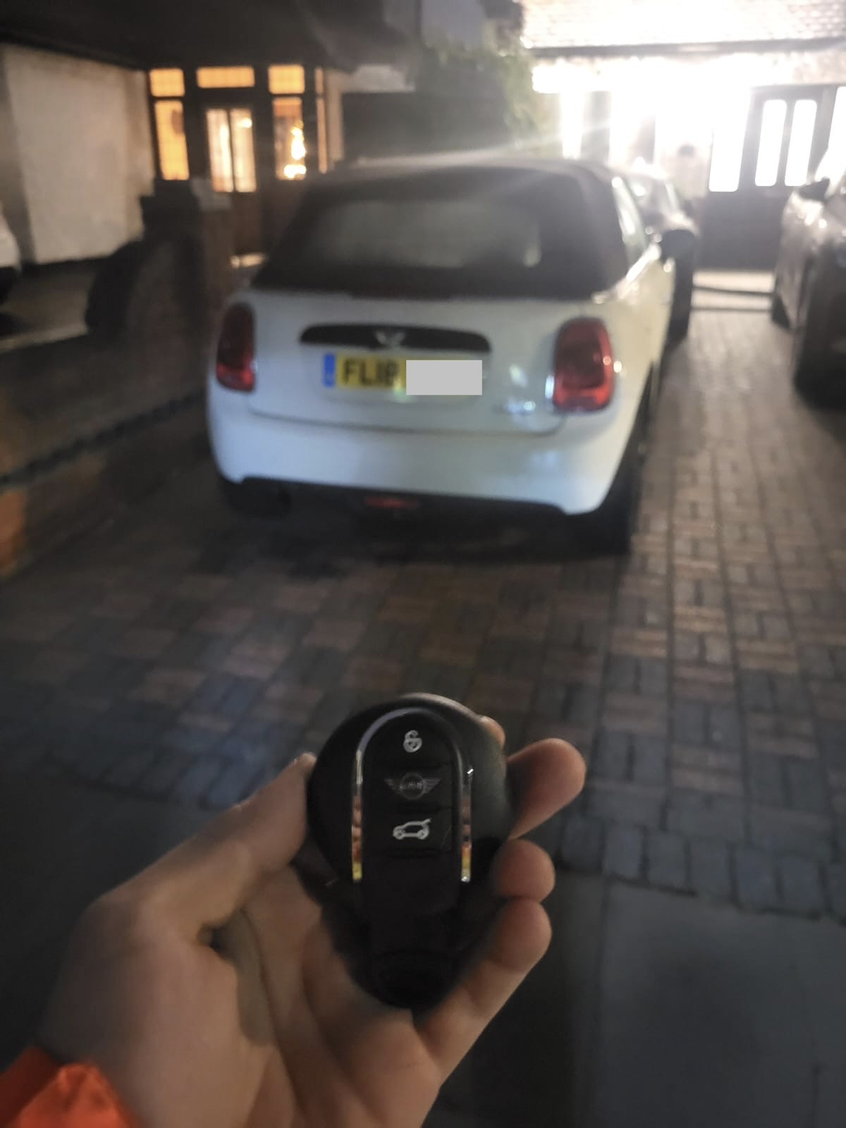 MINI proximity smart key held in front of a white MINI convertible on a block-paved driveway