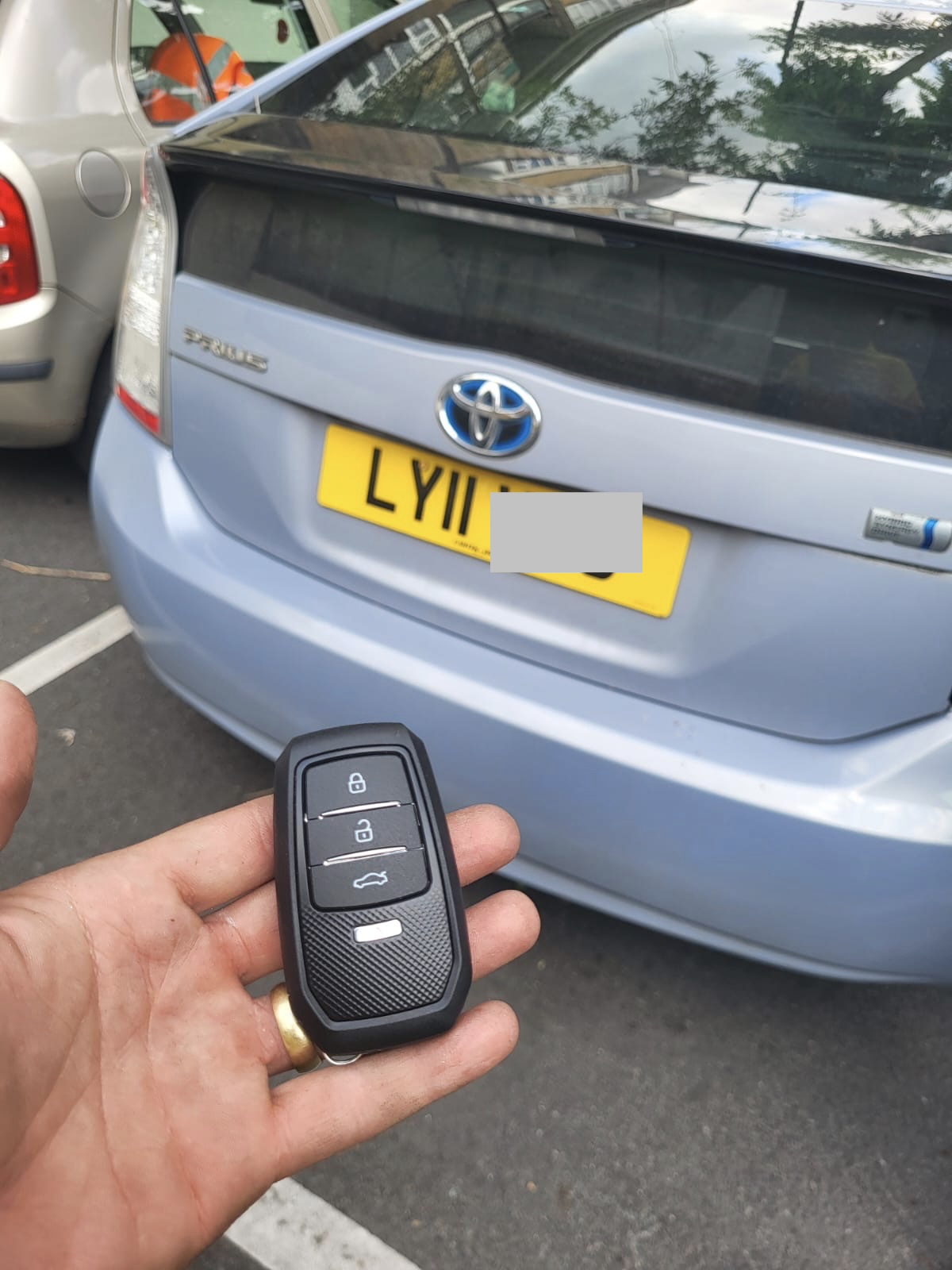 Toyota smart key held in front of a light blue Toyota Prius in a car park