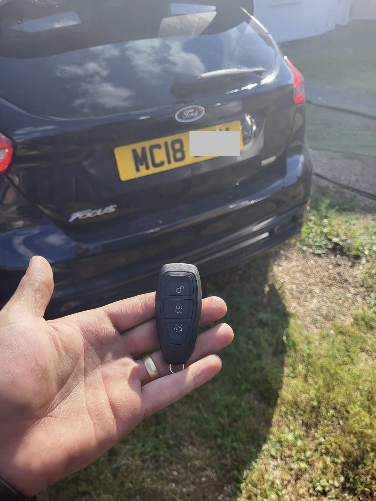 Three-button Ford keyless smart key held in front of a dark blue Ford Focus estate