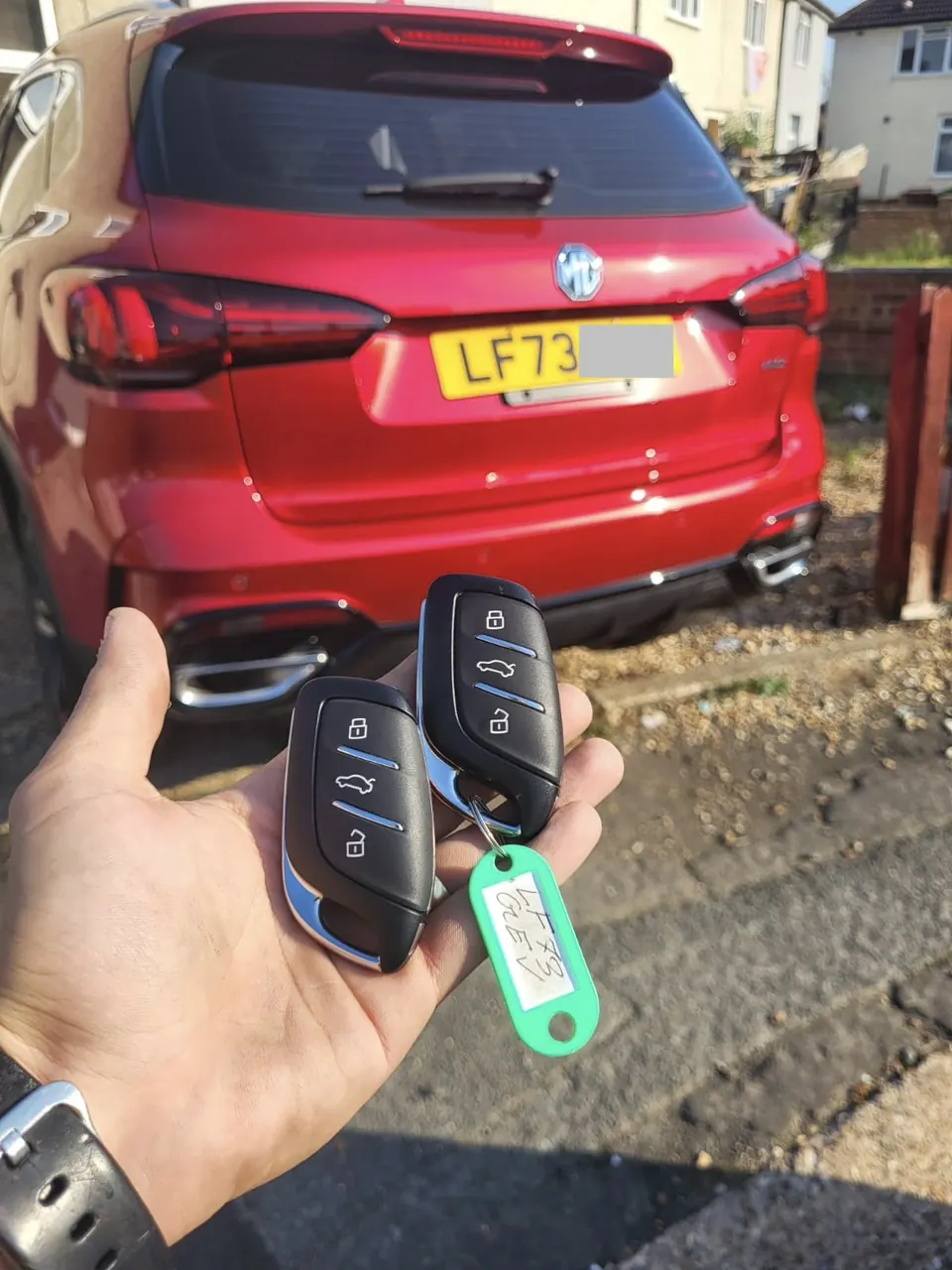 Two newly cut and programmed MG remote keys held in front of a red MG HS on a driveway