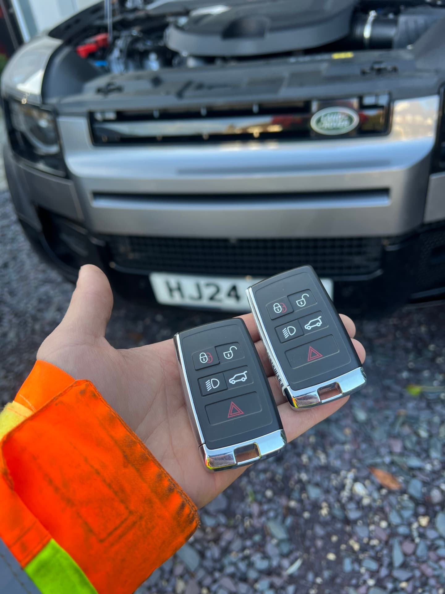 Two Land Rover smart keys held in front of a new silver Land Rover Defender