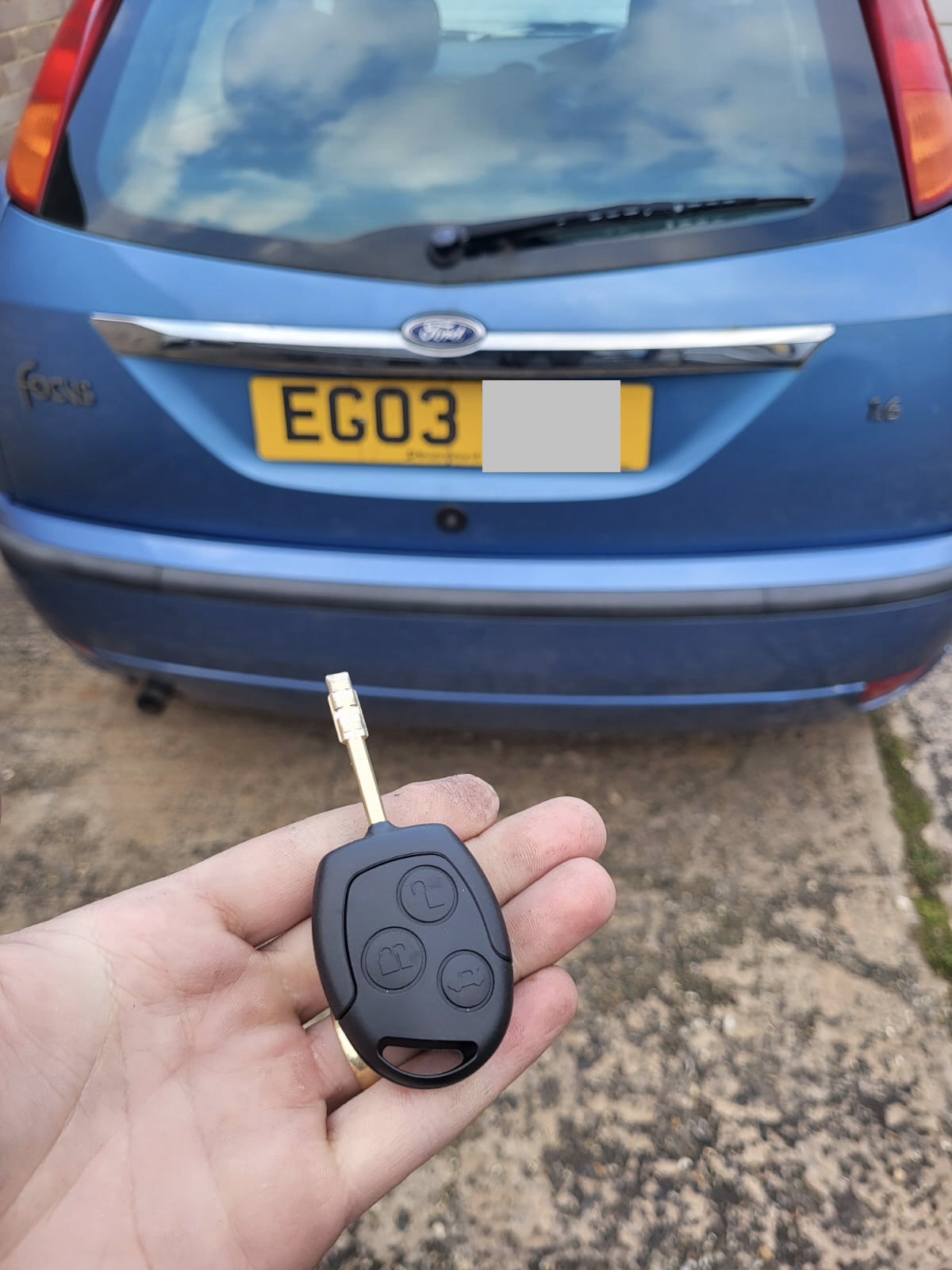 Ford three-button remote head key held in front of a blue Ford Focus