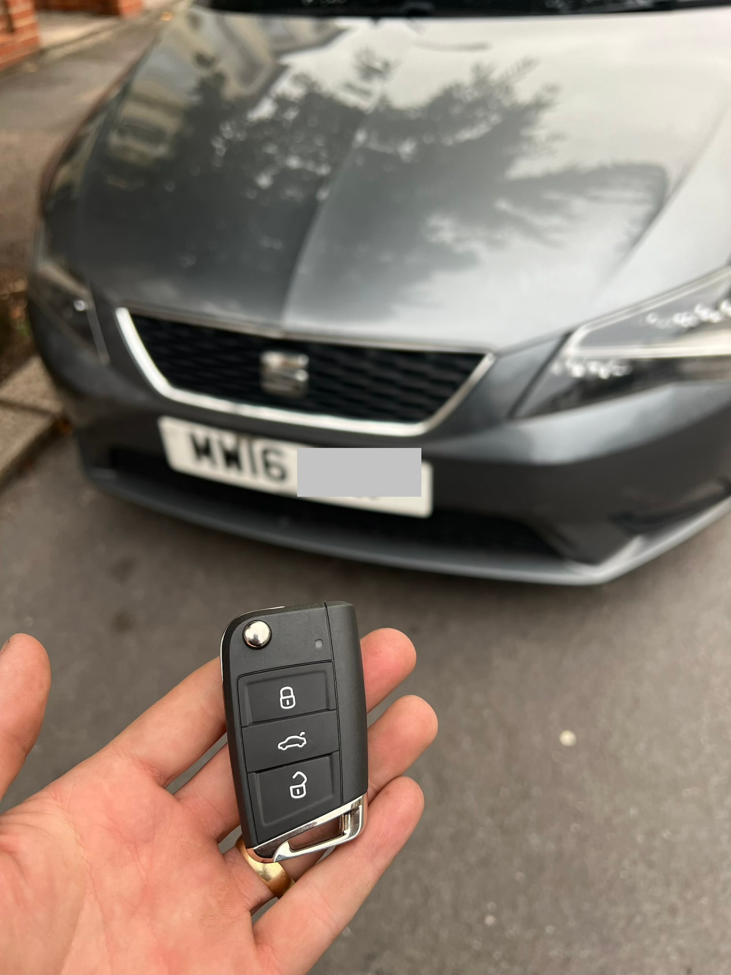 Seat flip remote key held in front of a grey Seat