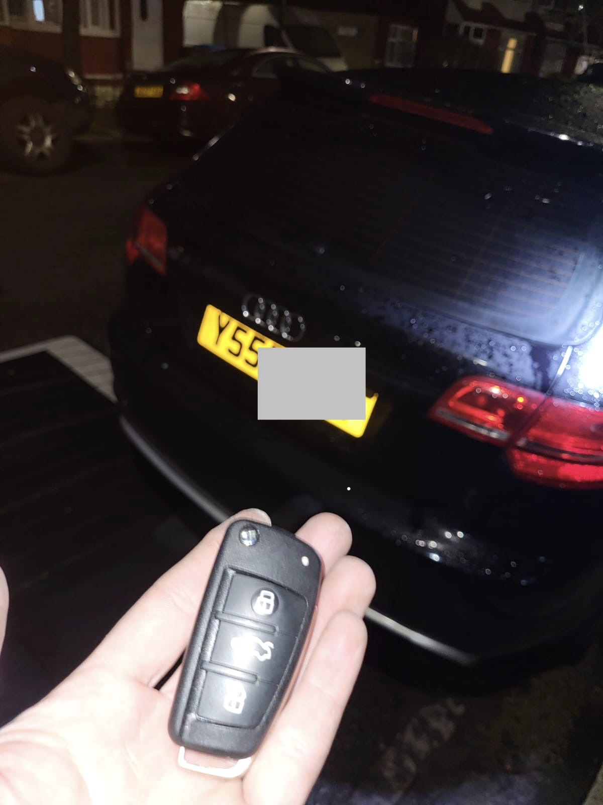 Audi three-button flip key held in front of a black Audi at night