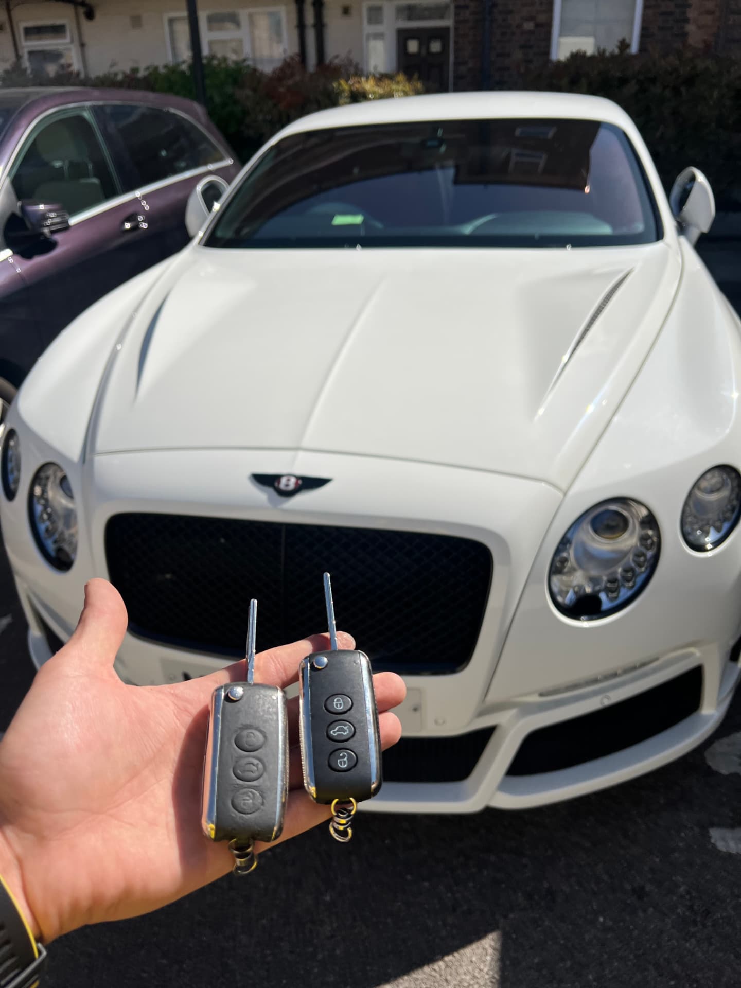 Two Bentley flip remote keys held in front of a white Bentley