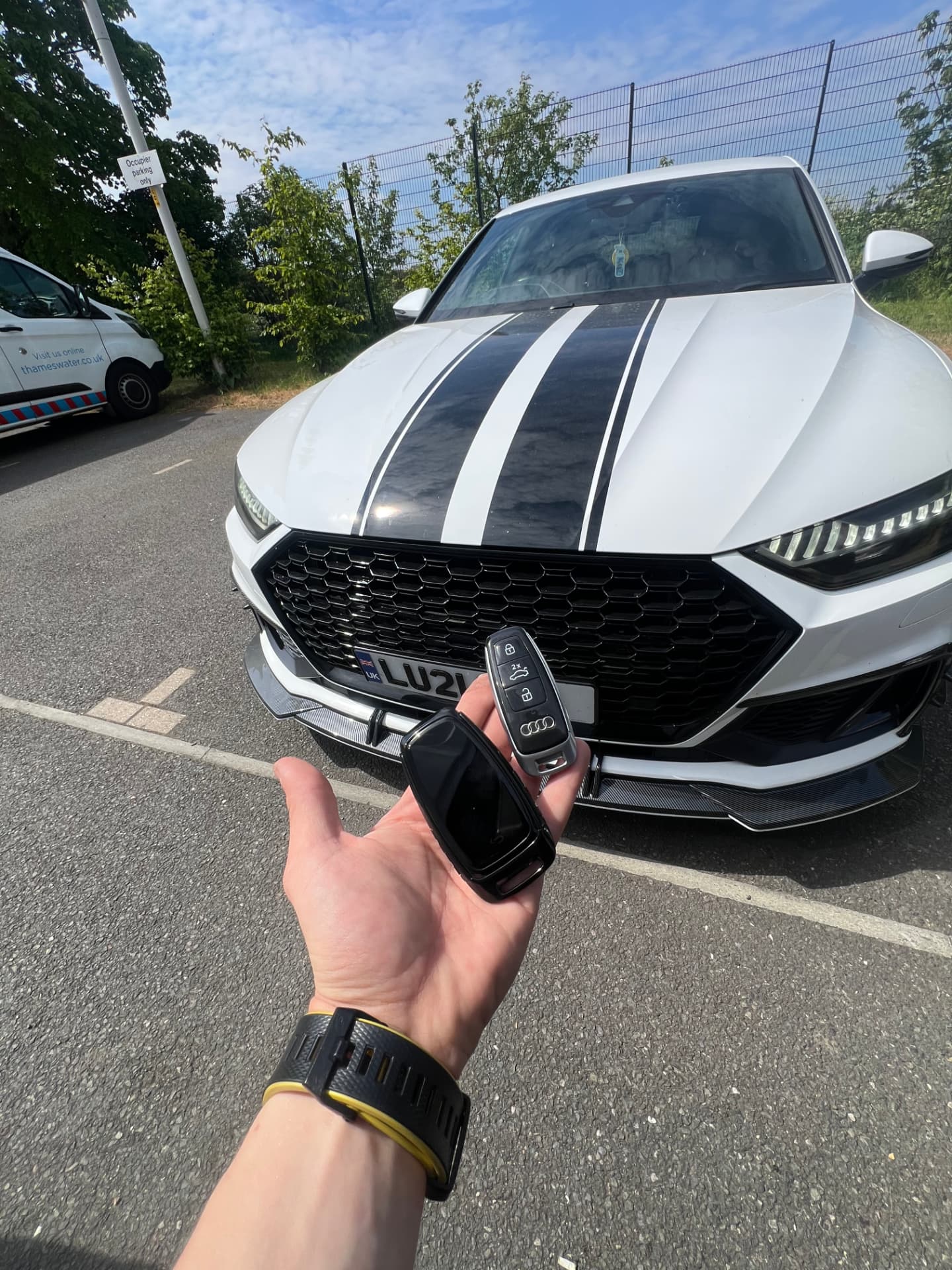 Two Audi smart keys held in front of a white Audi RS7 with black racing stripes
