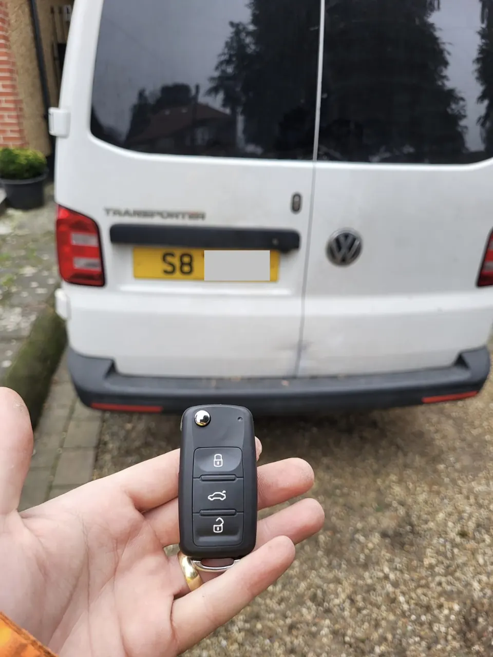 Volkswagen three-button flip key held in front of a white Volkswagen Transporter van