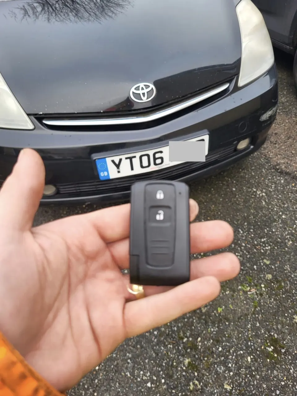 Toyota smart key card-style remote held in front of a black Toyota Prius