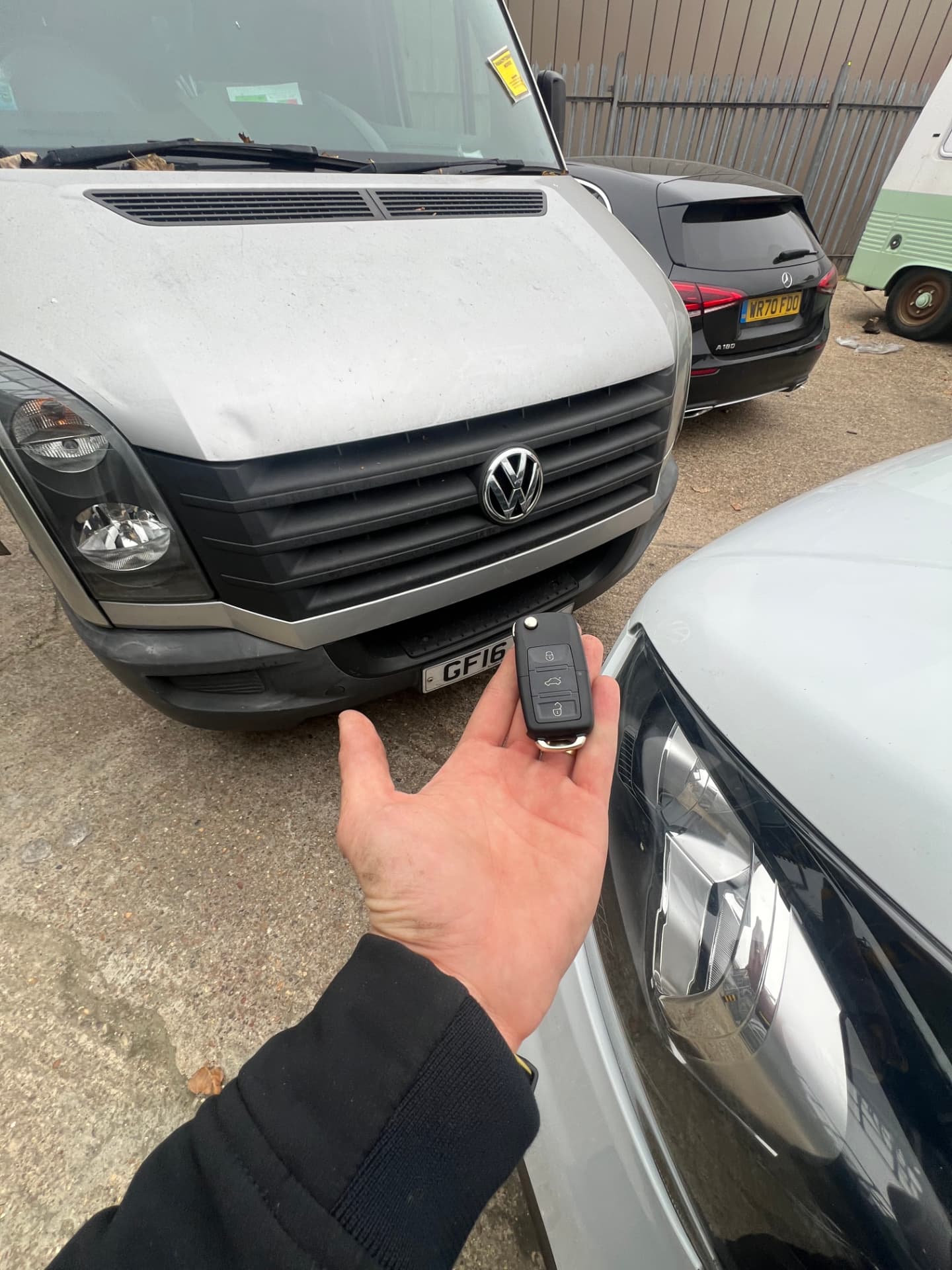 Volkswagen flip key held in front of a silver VW Crafter van in a yard