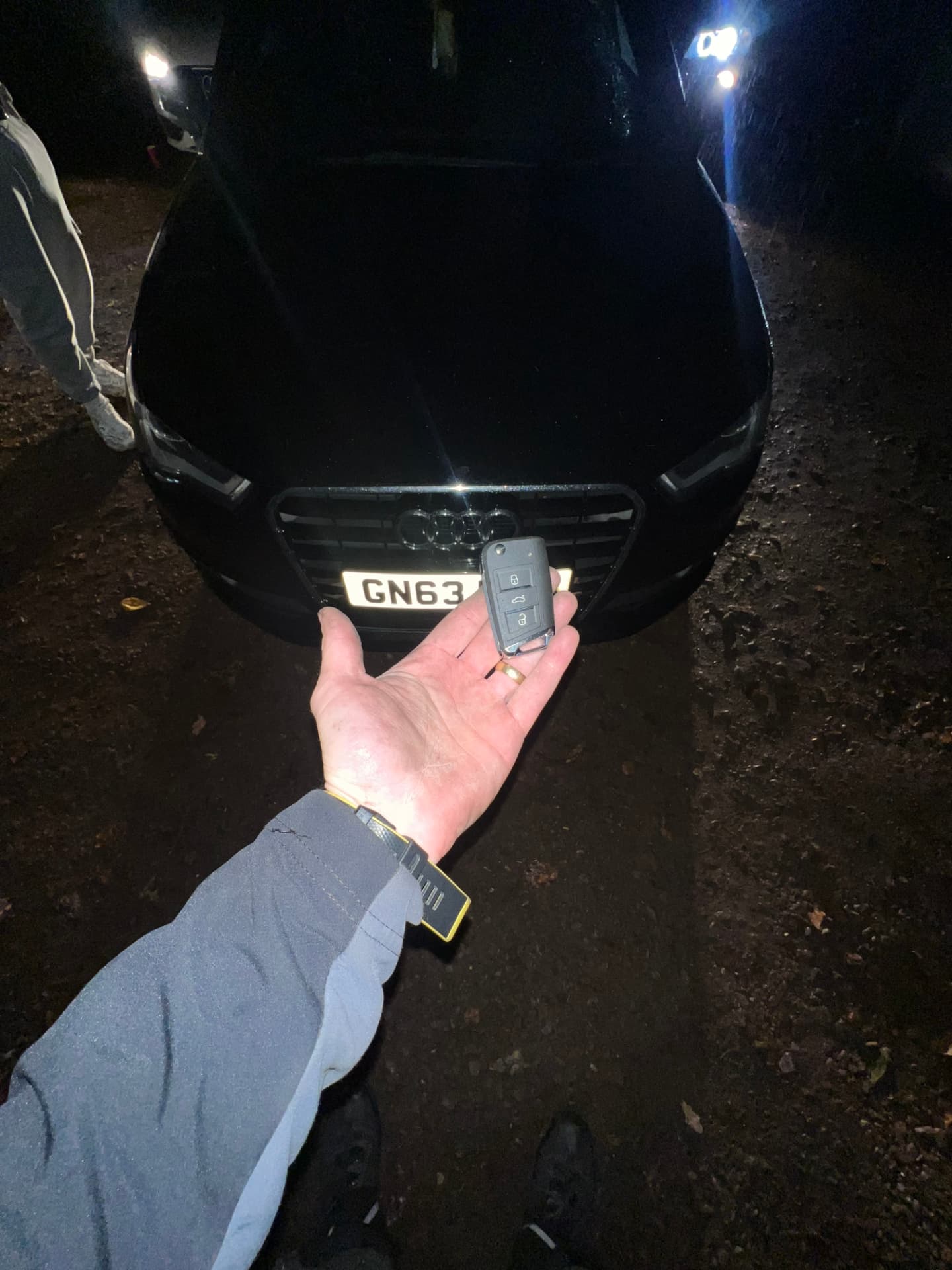 Audi flip key held in front of a black Audi A3 on an unlit road at night